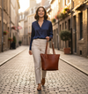 Woman walking down a cobblestone street holding a brown leather tote