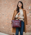 Woman holding a red vegan leather tote against a brick wall