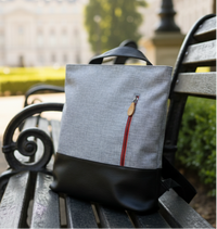 Gray convertible 3-in-1 backpack tote bag with a red zipper on a wooden bench in an outdoor setting