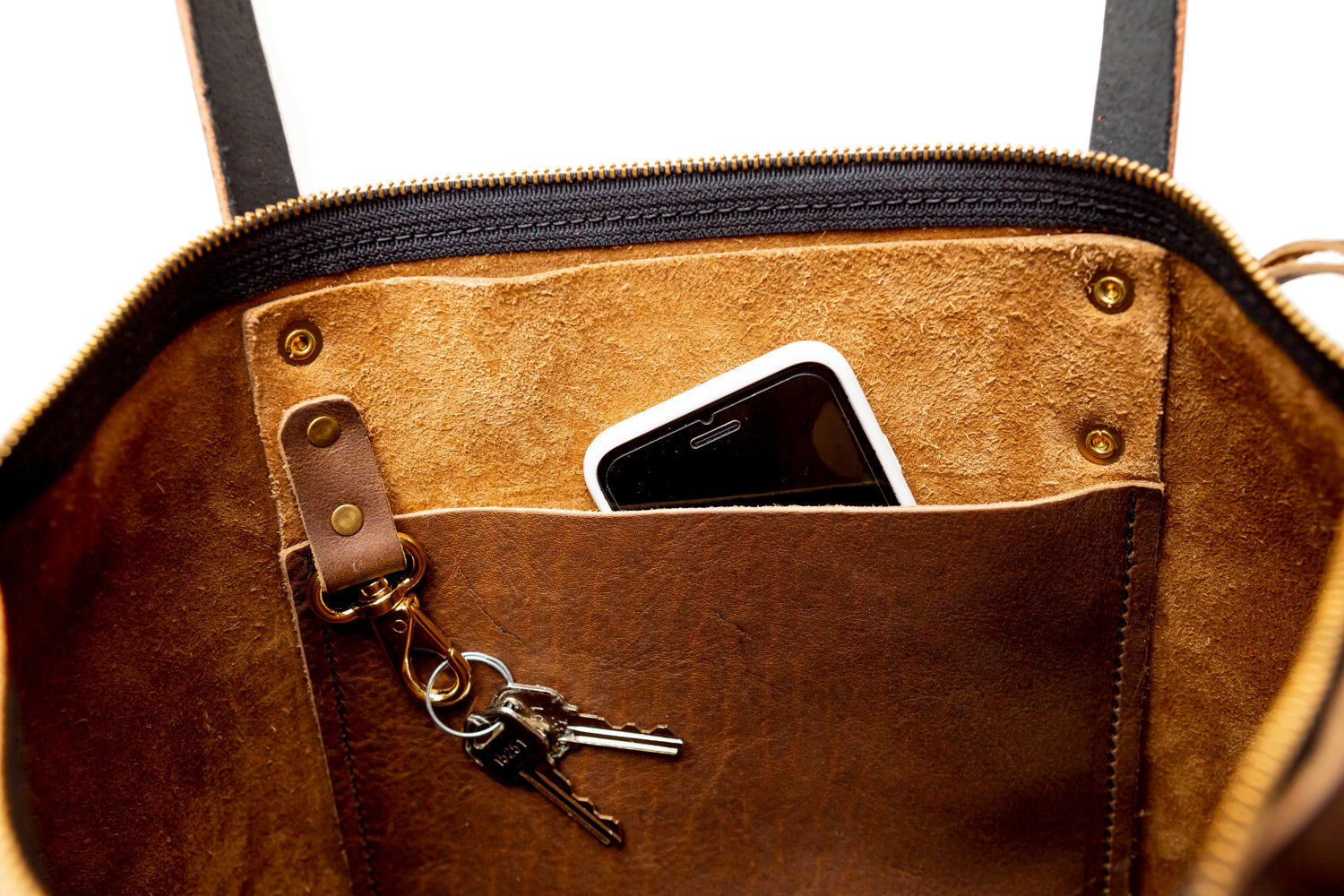 Inside of a brown leather tote with a pocket containing a phone and keys on a white background